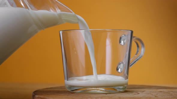 Close up Milk poured into glass from jar on wooden board with color background. Close up. 4k