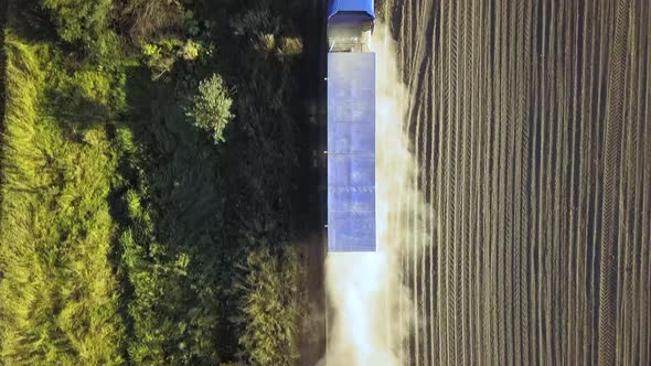 Aerial view of a truck driving on dirt road between plowed fields making lot of dust.