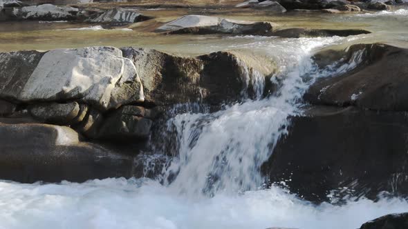 Wild mountain river flowing with stone boulders and stone rapids.