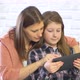 Happy mother and her daughter smiling having fun using digital tablet sitting on white sofa at home - VideoHive Item for Sale