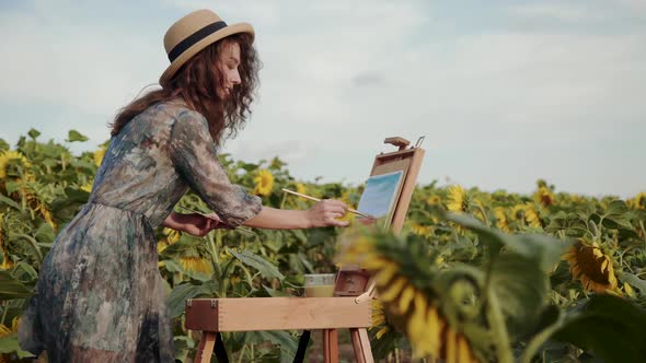 Cheerful Lady with Blowing Red Hair Painting Landscape Among Sunflowers