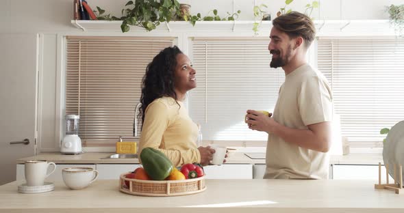 Happy Multiethnic Heterosexual Young Couple Having Coffee or Tea in Apartment