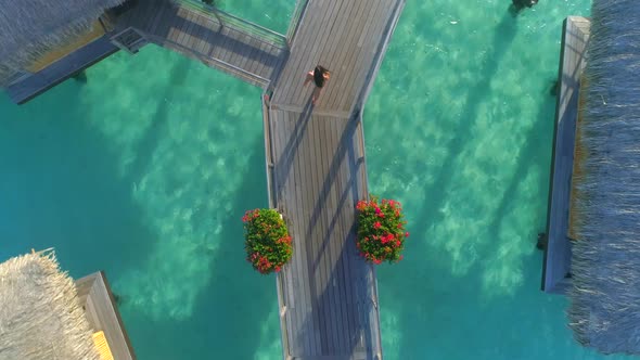 Aerial drone view of a woman walking between the overwater bungalows in Bora Bora tropical island.