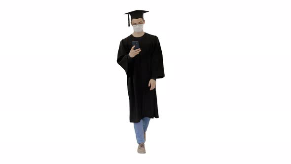 Young Man with Graduation Gown Walking in Medical Mask Using Smartphone on White Background.