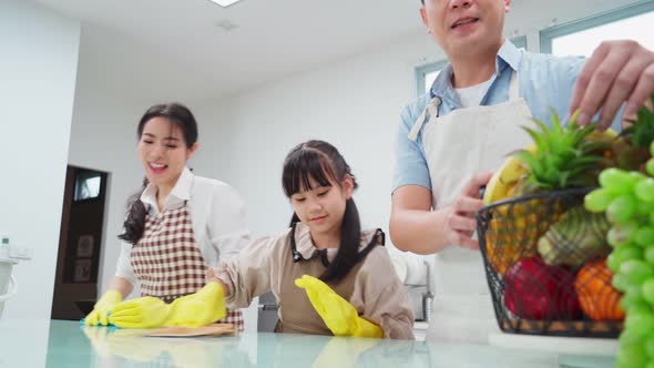 Asian young happy family teaching their daughter to clean kitchen counter with happiness in house.