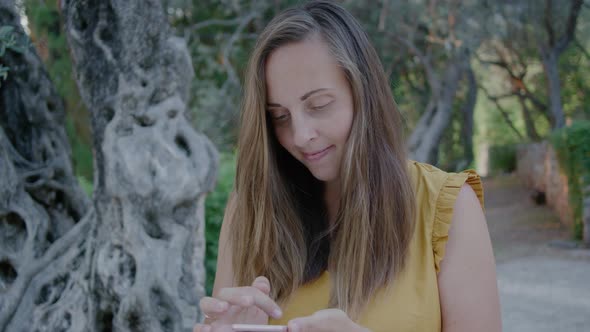 Pretty Woman in a yellow t-shirt reads a message on the phone against the background of nature