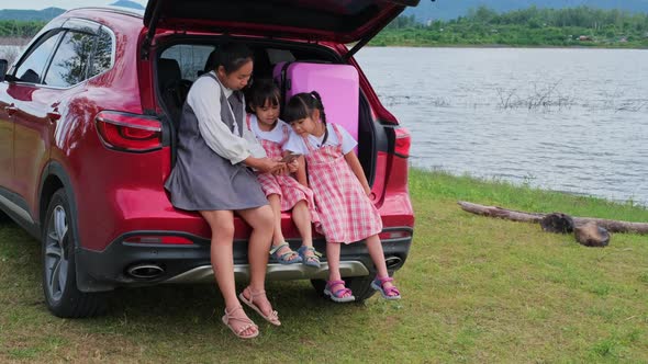 Asian mother watching a video with her children on a smartphone sitting together in the back.