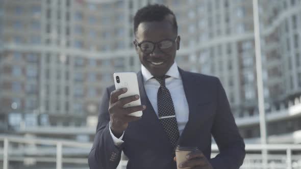 Smiling Confident African American Man in Formal Suit and Eyeglasses Using Smartphone Outdoors