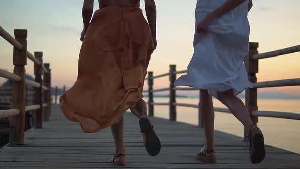 Low Angle View of Girls in Summer Dresses Running Along the Wooden Pier Friends Having Rest on