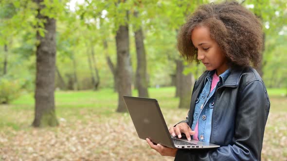 Young African Beautiful Girl Works with Notebook in the Forest - She Look for Right Words