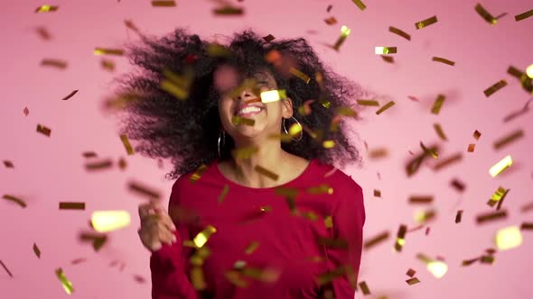 Beautiful african woman having fun smiling and dancing under confetti rain in studio