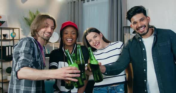 Friends which Clinking Bottles of Beer while Looking at Camera During Home Party
