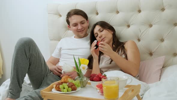 Happy Couple Having Fun Eating Breakfast in Bed and Drinking a Cup of Coffee