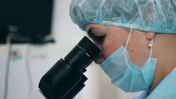 Woman Works with Microscope at a Hospital.