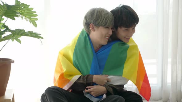 Asian loving gay couple cuddling, putting on LGBT rainbow flag to cover shoulder