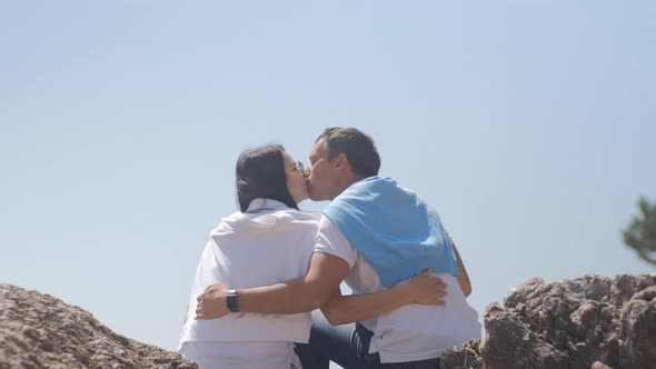Romantic couple sit and embrace near the sea. Man and woman with black hair spend vacation