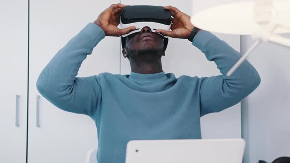 Black Man Wearing a Virtual Reality Glasses Sitting at the Table with His Laptop