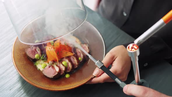 Waiter Serving Meat Dishes with Smoke to a Client in a Restaurant