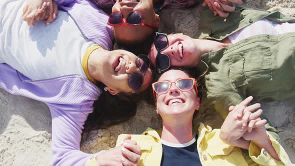 Happy group of diverse female friends having fun, holding hands and smiling at the beach