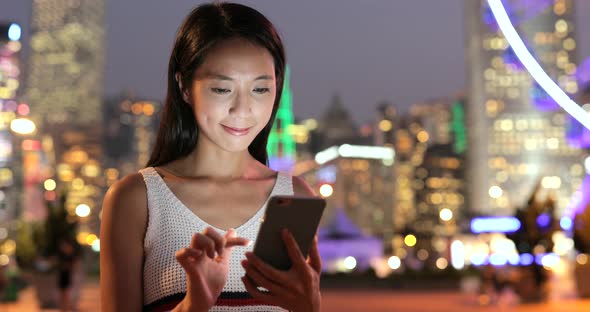 Woman looking at mobile phone in the city at night 