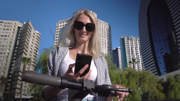 a woman uses app in her smartphone to rent electric scooter.