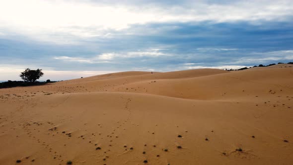 Aerial forward view of red sand dunes with a timeless atmosphere and girl running in the distance. M