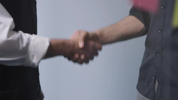 Handshake of Caucasian and Middle Eastern Men Behind Glass Door in Meeting Room