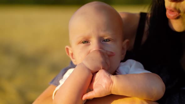 Baby sucking fingers on hands of mother in rural landscape