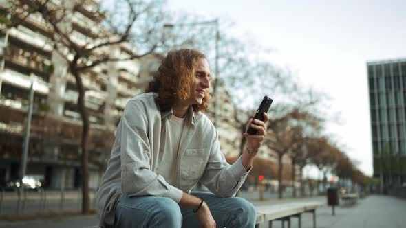 Smiling curly-haired man texting by mobile