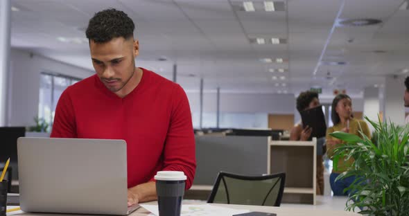 Biracial businessman using laptop over business colleagues in office