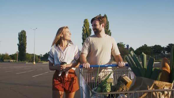 Female and Male Smiling and Talking Walking By Empty Parking Lot with Trolley of Groceries After