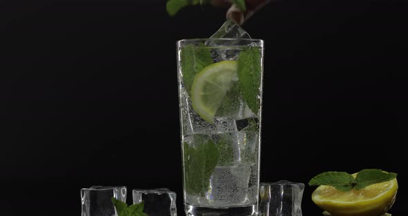 Clear Water in Glass with Green Mint Leaves and Ice Cubes on Black Background