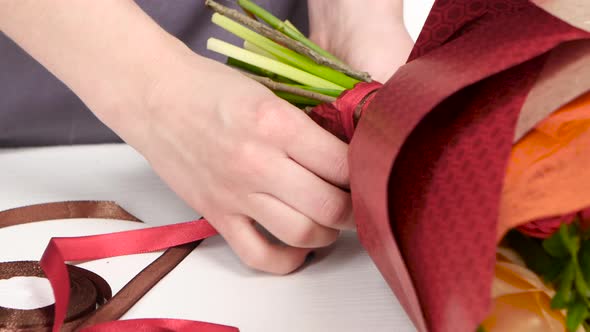 Florist Tying a Bow of Ribbon on a Bouquet of Flowers. White. Close Up