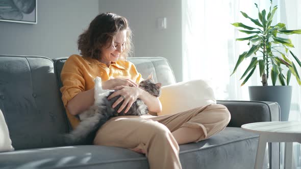 A Young Adult Woman Stroking a Grey Fluffy Cat While Sitting on the Couch