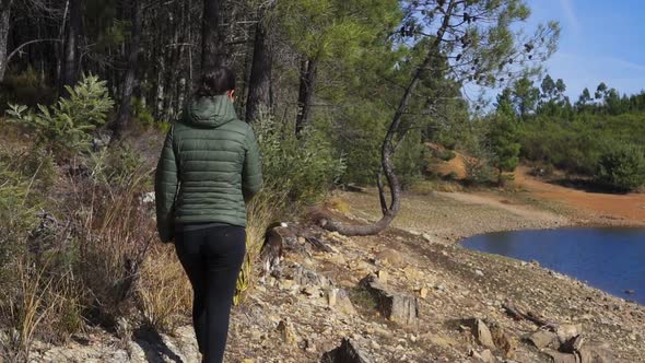 Caucasian woman with green jacket walking a dog on a path