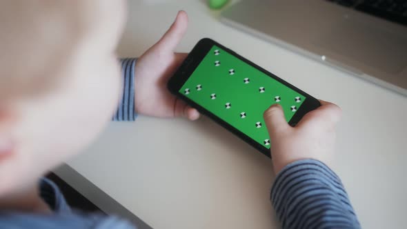 Kid Boy Using Smartphone with Green Mockup Screen Playing Game or Browsing Internet on Phone