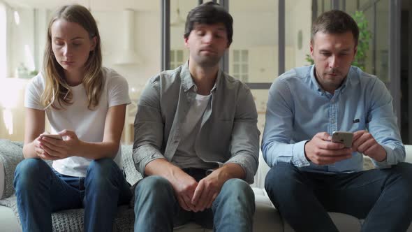 Bored Man Sitting on Couch Between Gadget Addicted Friends with Smartphones