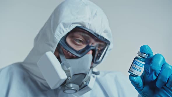 Scientist in a Protective Suit, Goggle and Respirator Holding a Vaccine.