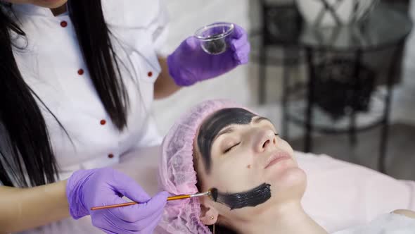 doctor cosmetologist applies a black mask with a brush to cleanse and moisturize the skin