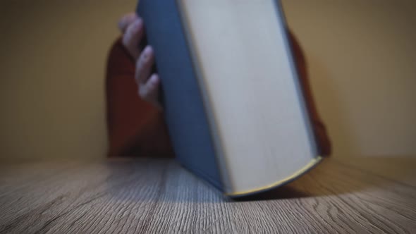 Woman opens book on a wooden table and starts reading - Slow Motion