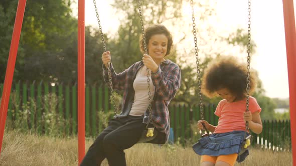 Two Cheerful Sisters Moving Back and Forth on Swings, Outdoor Child Playground