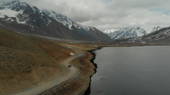 Aerial View Of SUV Driving Going Along Winding Road Beside Shandur Lake In Pakistan. Dolly Forward