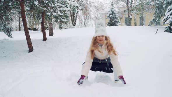 Pretty girl is playing with snow in the park in winter.