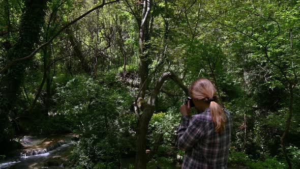 Woman taking pictures of a beautiful waterfall in green spring forest