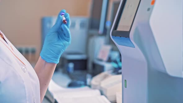 Laboratory worker holds a vial and mixes it by hand in hospital.