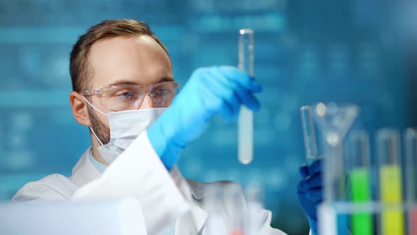 Male Chemical Technician Wearing Medical Protective Mask and Glasses Holding Tube with Substance