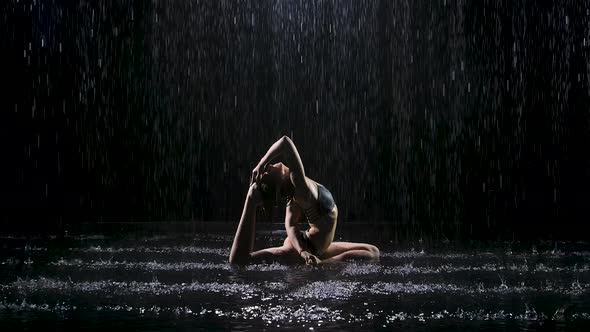 Beautiful Young Woman with Dark Hair in Dove Pose Under the Streams of Rain. The Studio Light