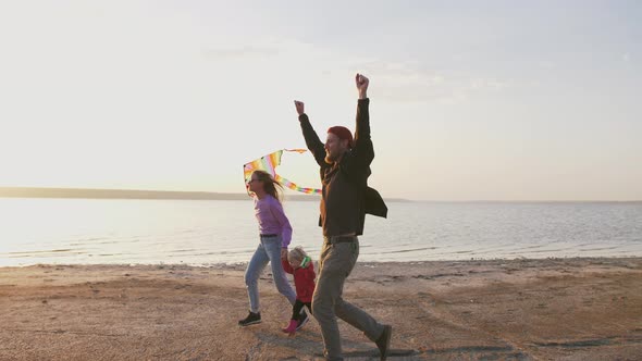 Happy Family Running and Having Some Fun with Flying Kite at the Seashore During Sunset Slow Motion