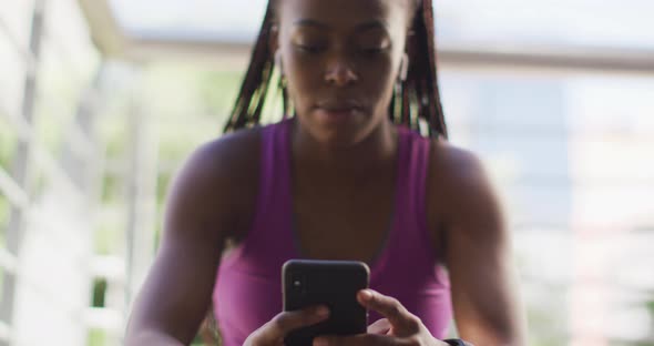 African american woman smiling while using smartphone sitting on the stairs of the city bridge