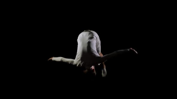 Handsome Male Gymnast in White Clothes on a Black Background Jumping on a Trampoline in Slow Motion